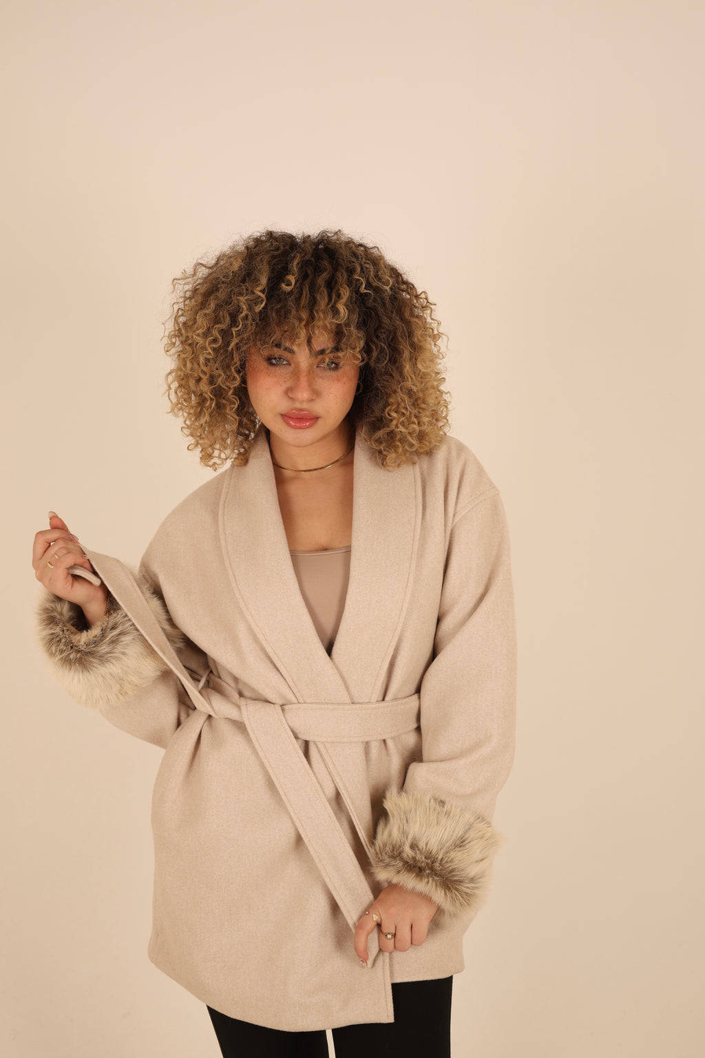 Woman wearing a beige coat with fur cuffs and collar against a beige background