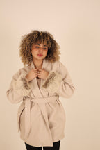Woman wearing a beige coat with fur trim on a plain background