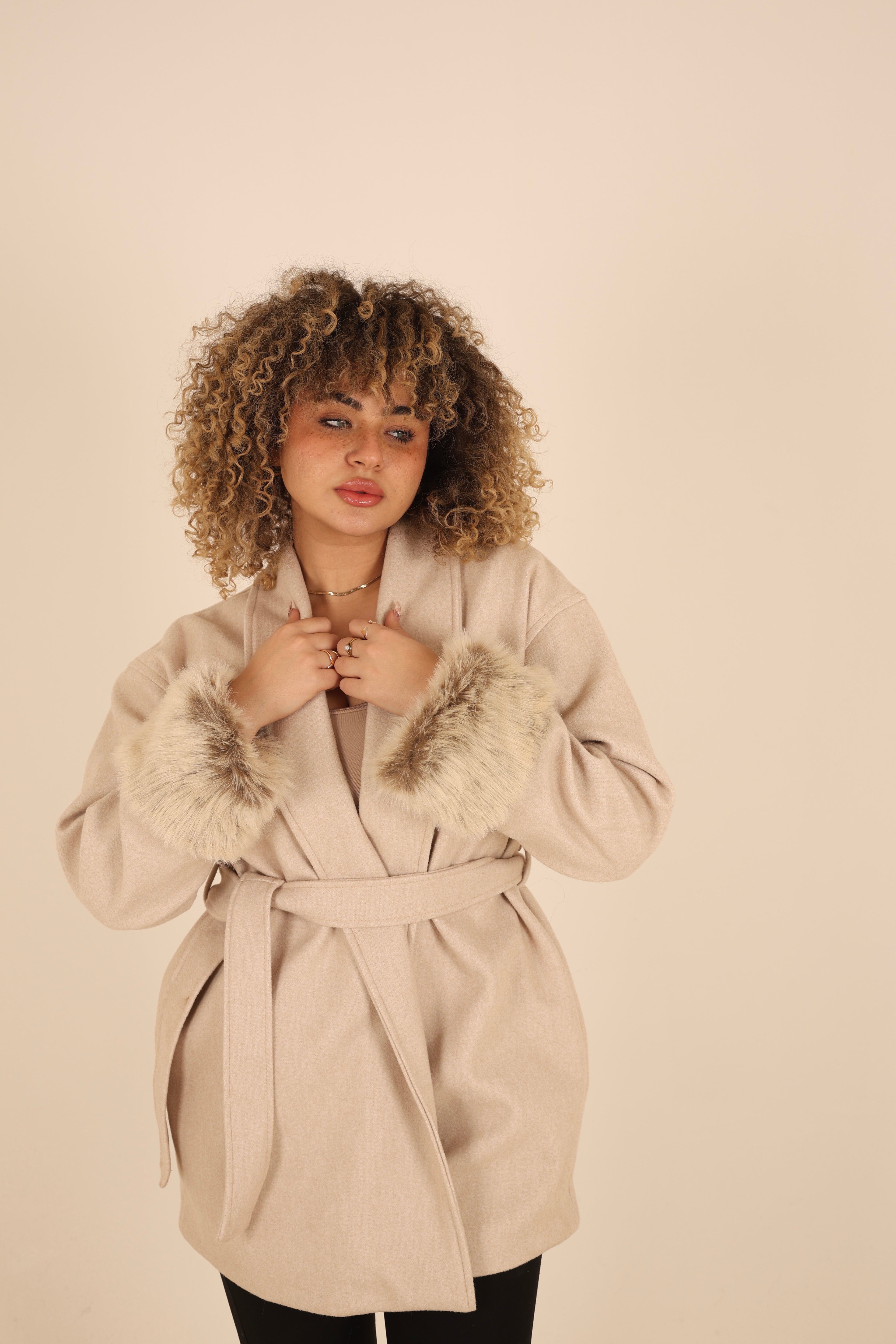 Woman wearing a beige coat with fur trim on a plain background