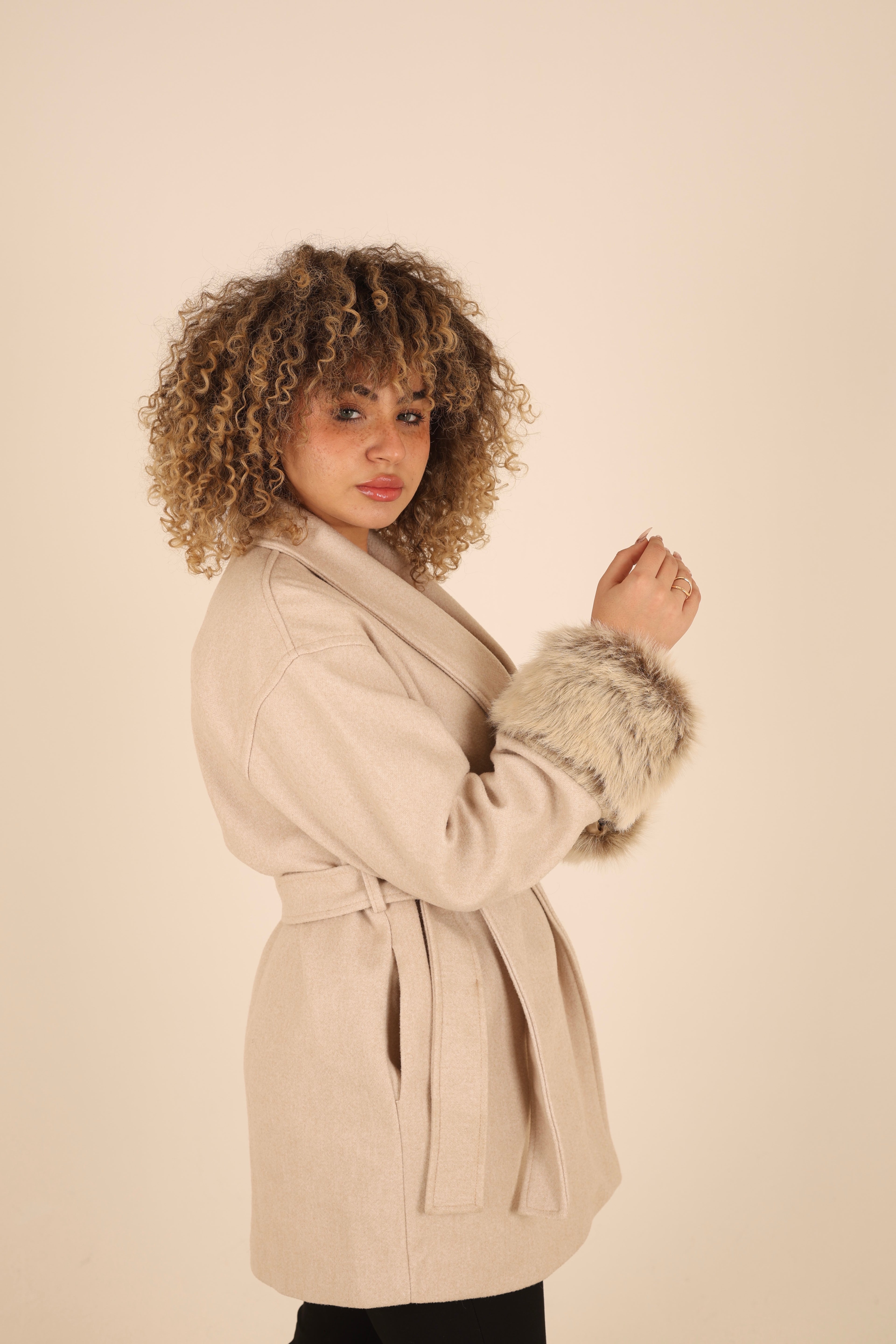 Woman wearing a beige coat with fur cuffs on a beige background