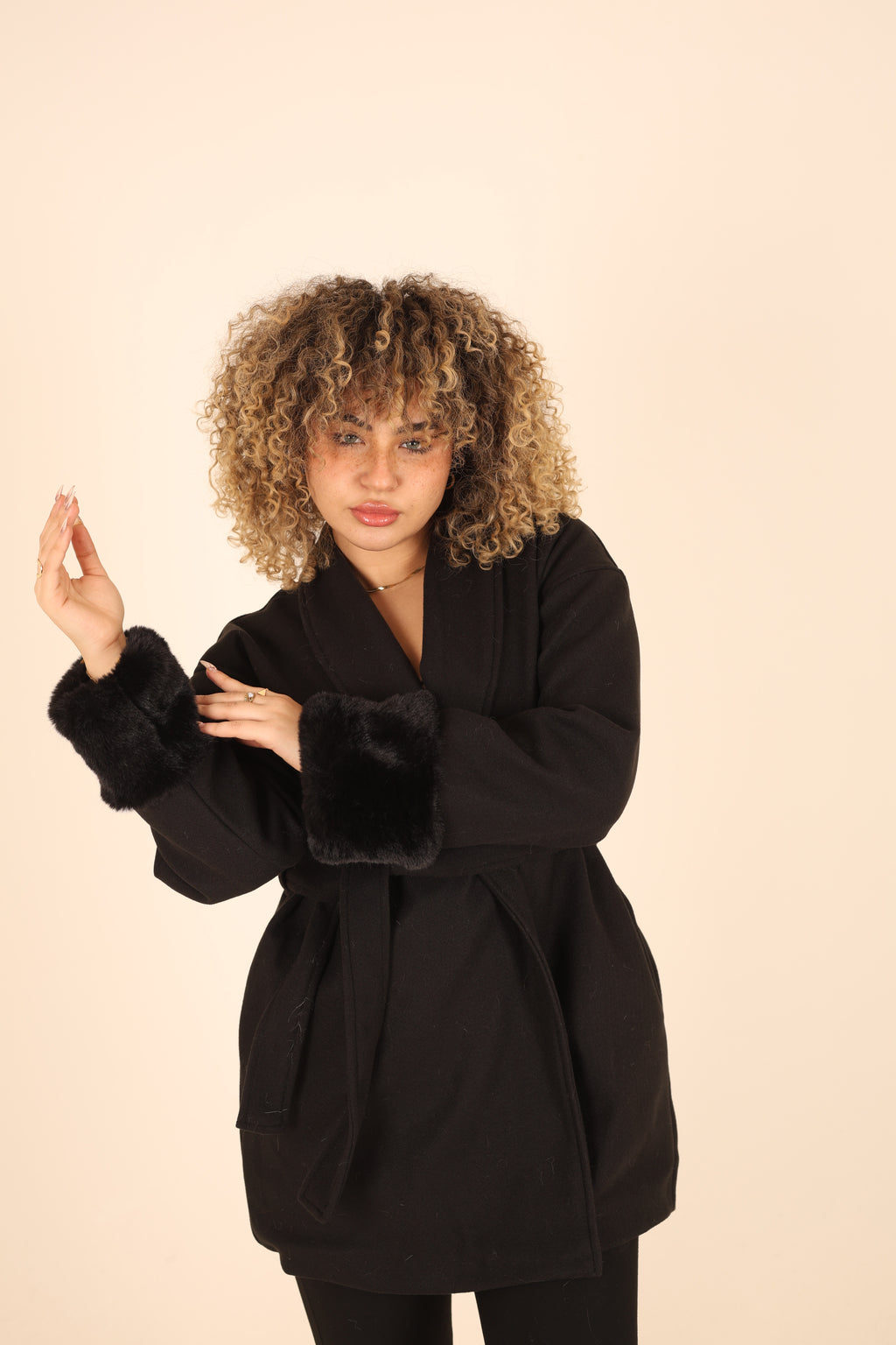 Woman wearing a black coat with fur trim on a beige background