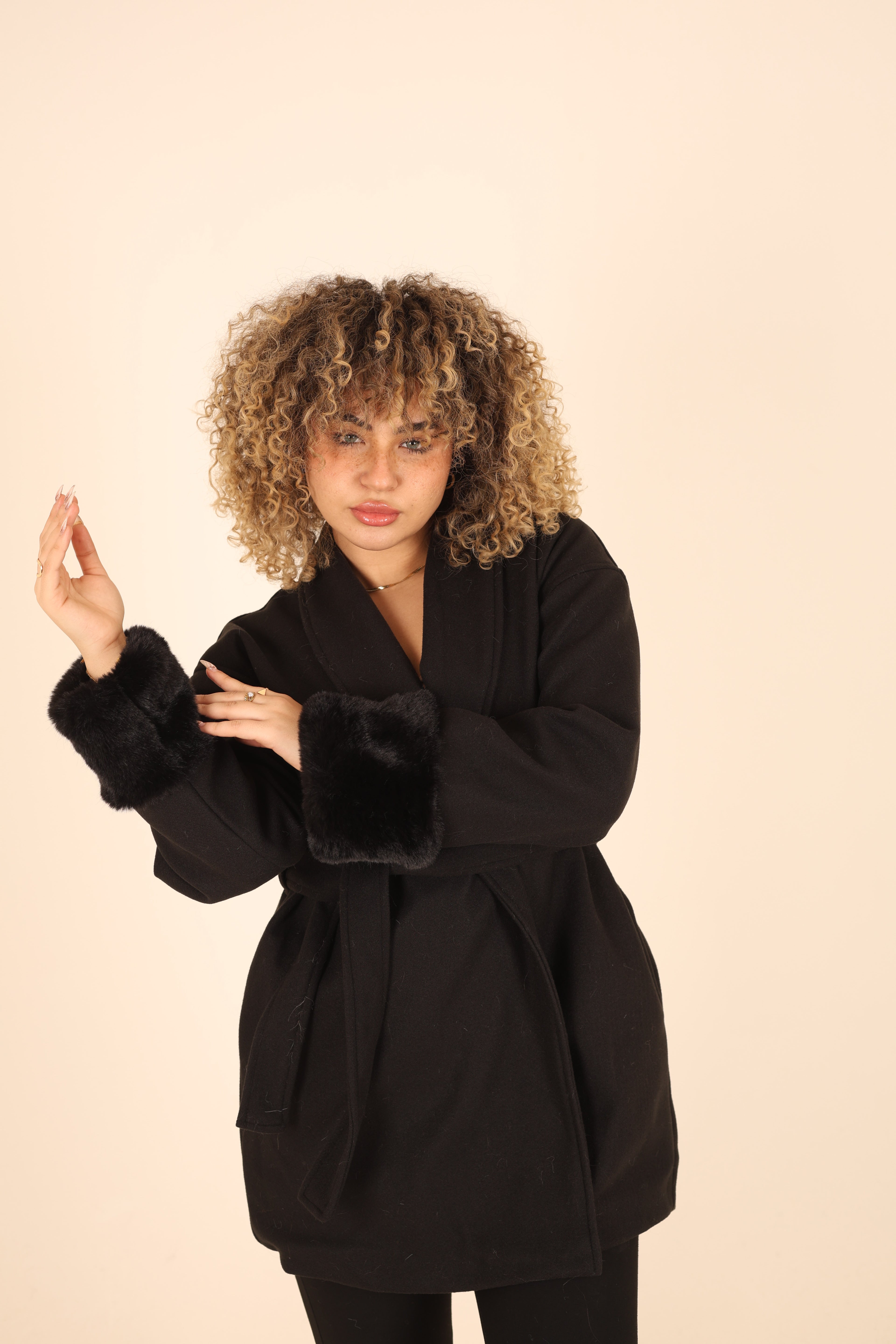 Woman wearing a black coat with fur trim on a beige background