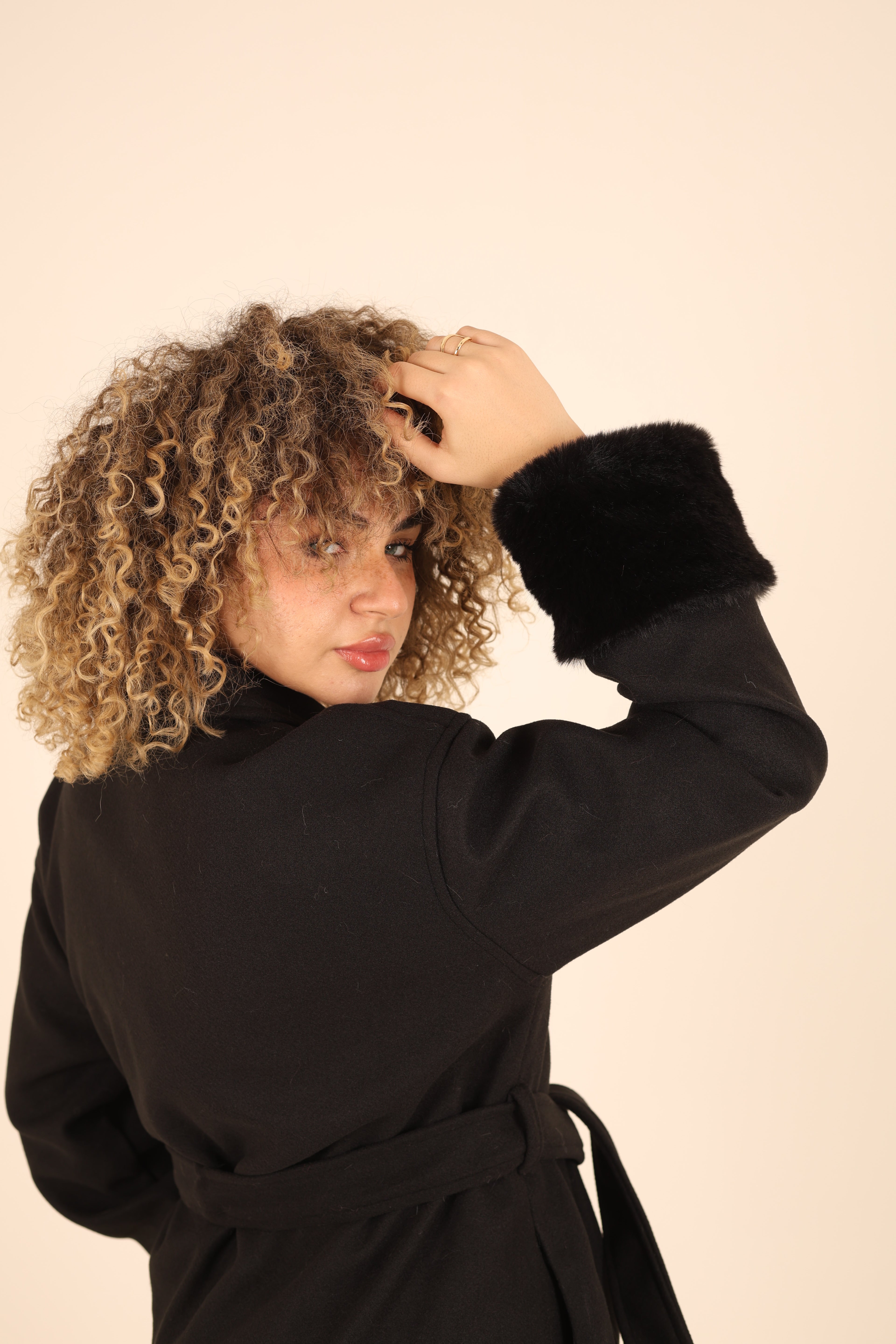 Person wearing a black coat with a hood on a beige background