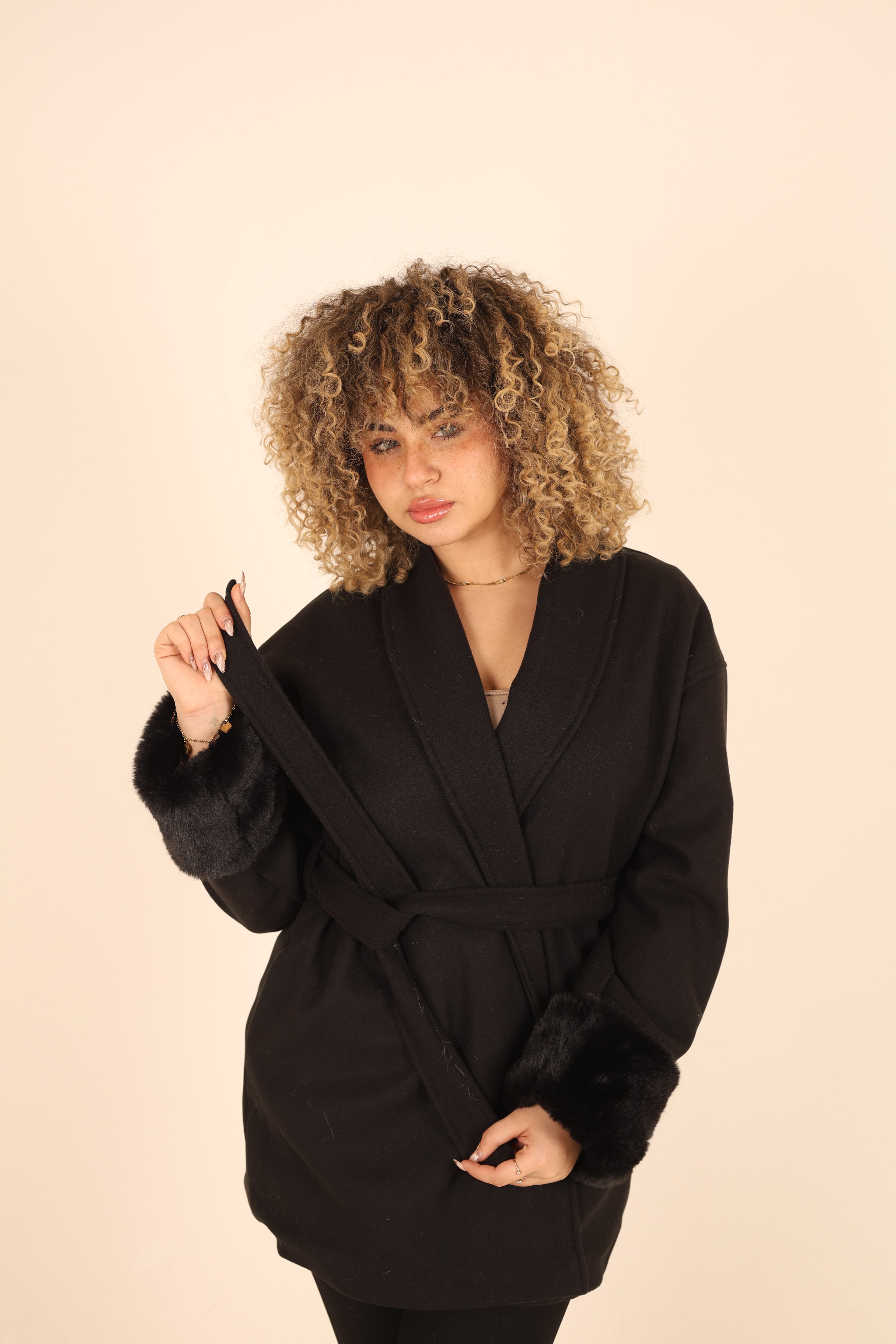 Person wearing a black coat against a beige background